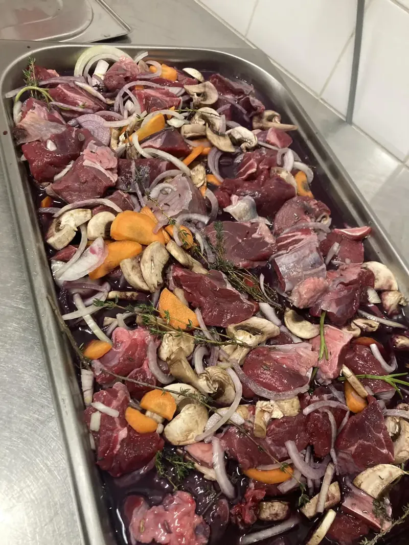 Morceaux de viande marinés au vin rouge avec carottes, champignons, oignons et thym, dans la cuisine du restaurant